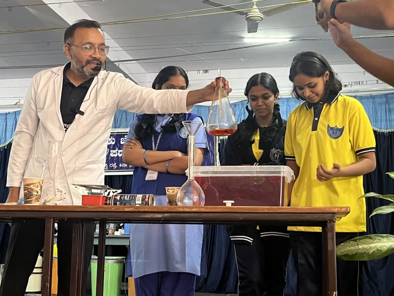 A Manthan educator demonstrates a chemistry experiment with students on stage