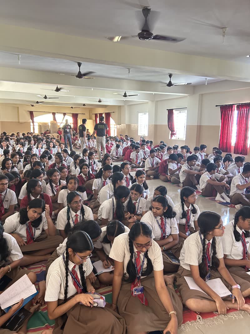 Students seated on the floor of a school hall watching Manthan