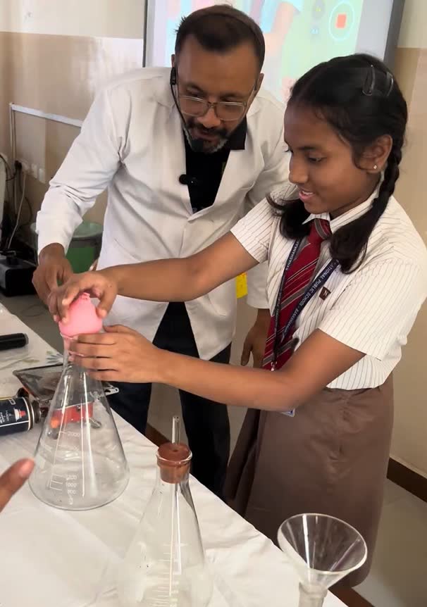 A student pours liquid into a conical flask guided by an educator