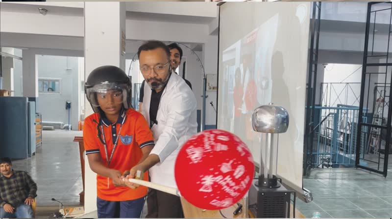 Student in a helmet holding a balloon near a Van de Graaff generator