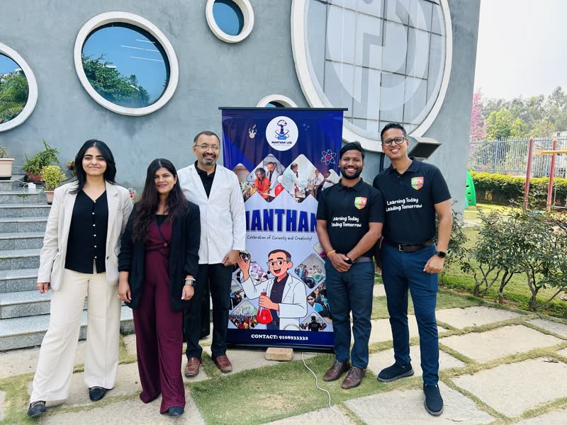 The Manthan team standing beside the Manthan banner at a school