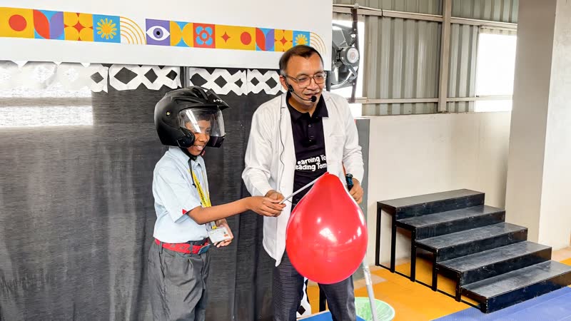 A student wearing a helmet touches a balloon to a Van de Graaff generator